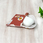 Load image into Gallery viewer, Open daisy print AirPods pouch with white earbuds case inside, placed on light wood surface with green leaves in the corner
