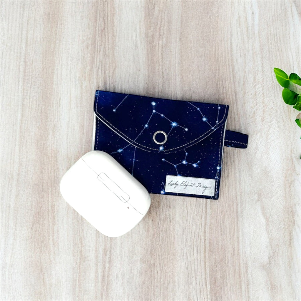 Navy blue constellation print AirPods pouch with white earbuds case on light wood background
