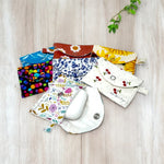 Load image into Gallery viewer, Assorted colorful fabric AirPods cases with snap closures in various floral and patterned designs on a light wood surface
