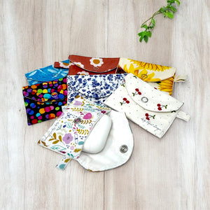 Assorted colorful fabric AirPods cases with snap closures in various floral and patterned designs on a light wood surface