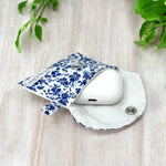 Load image into Gallery viewer, White and blue floral fabric AirPods case pouch with snap closure on light wooden surface
