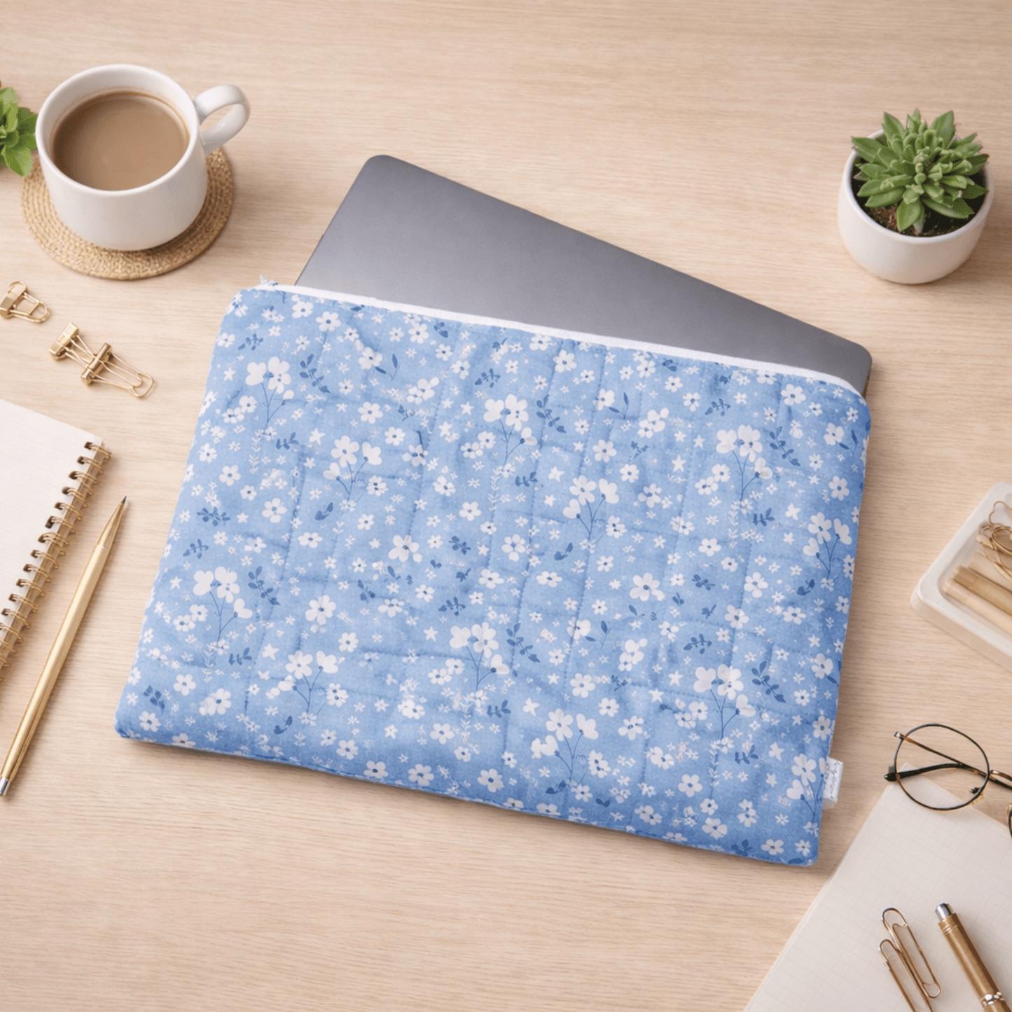 Blue floral quilted laptop sleeve on desk with laptop and accessories, padded case for stylish protection