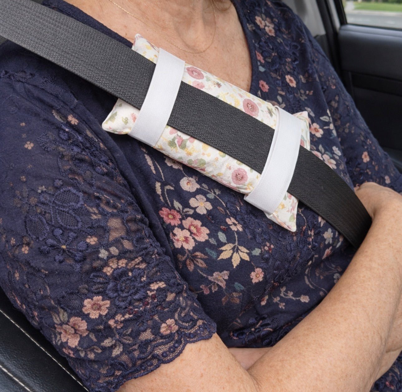 Woman wearing floral chemo port pillow attached to seatbelt providing chest protection and comfort during car rides after surgery or treatment