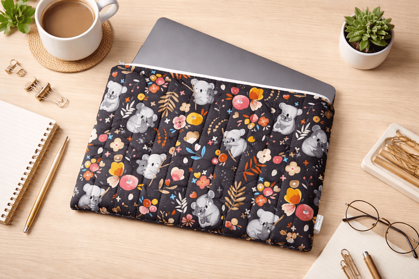Dark floral quilted laptop sleeve with padded protection on a desk with laptop, styled flatlay for everyday use