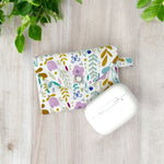 Load image into Gallery viewer, Closed floral fabric AirPods pouch with snap button and white wireless earbuds case on wooden surface with green leaves
